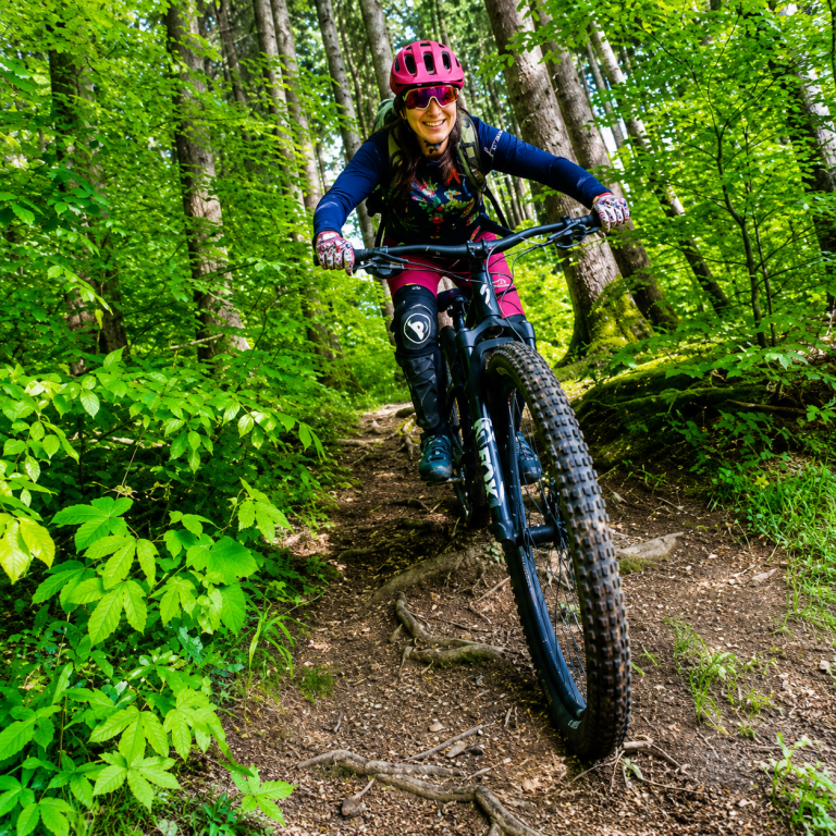 E-Mountainbikerin fährt im Techniktraining einen steilen Waldweg bergauf
